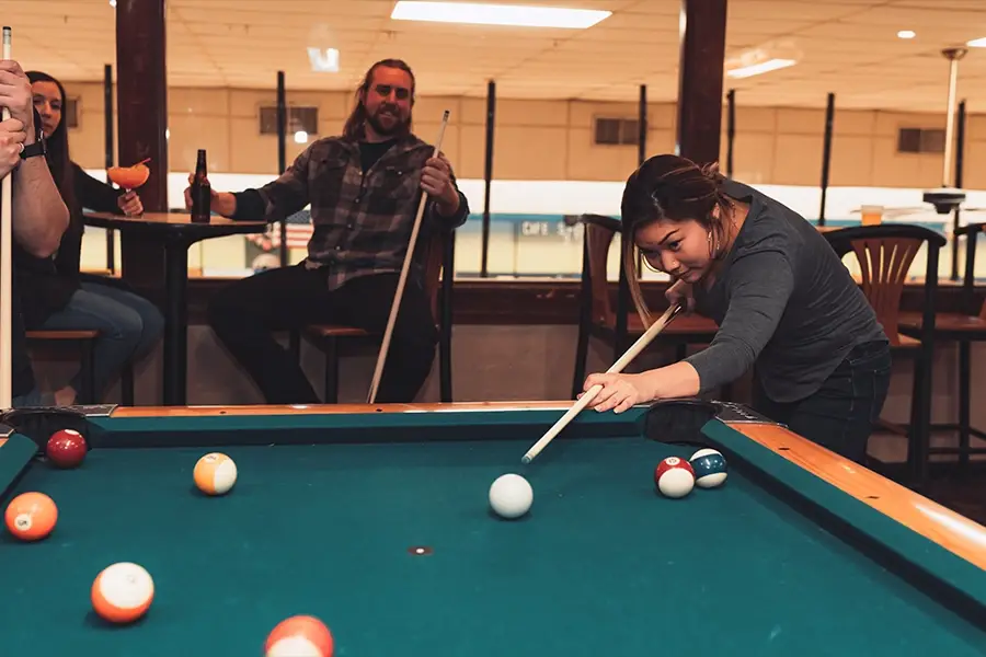 Woman lining up a pool shot while friends watch at St. Clair Bowl