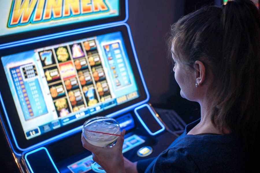 Woman holding a drink while playing an illuminated gaming machine